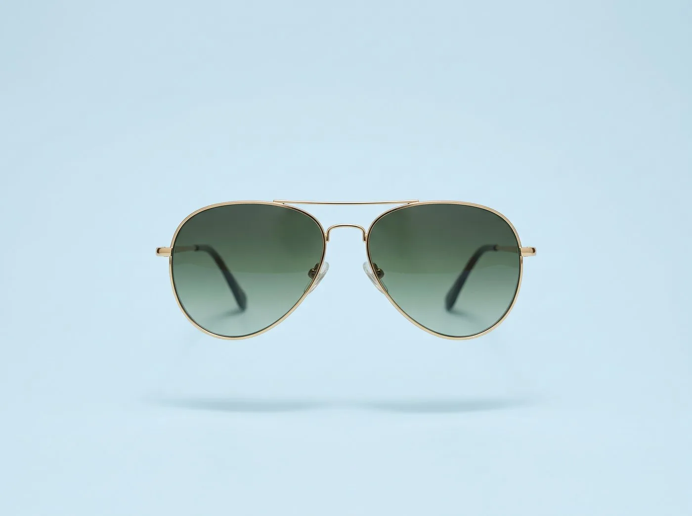 Occhiali da sole aviator oro con lenti verdi su fondo azzurro polvere